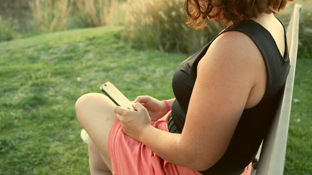 Mujer persona muchacha chica chava escribiendo en el celular haciendo anotaciones en su telefono texteando en el atardecer en el parque al aire libre descansando relajandose