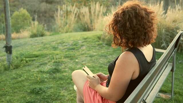 Mujer persona muchacha chica chava escribiendo en el celular haciendo anotaciones en su telefono texteando en el atardecer en el parque al aire libre descansando relajandose