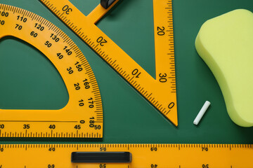 Protractor, triangle, ruler and sponge on green chalkboard, flat lay
