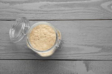 Leaven in glass jar on grey wooden table, top view. Space for text