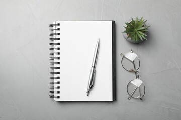 Ballpoint pen, notebook and glasses on light gray table, flat lay