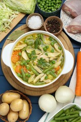 Saucepan of delicious vegetable soup with chicken and different ingredients on blue wooden table, flat lay