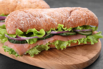 Delicious sandwich with fresh vegetables and salmon on wooden board, closeup