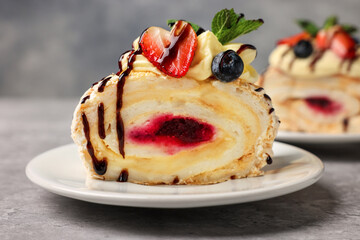 Piece of tasty meringue roll with jam, cream, strawberry, blueberry and mint on light grey table, closeup