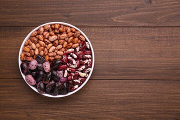 Different kinds of dry kidney beans in bowl on wooden table, top view. Space for text