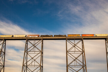 Train crossing a large metal bridge with clouds