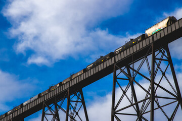 Fototapeta na wymiar Train crossing a large metal bridge with clouds