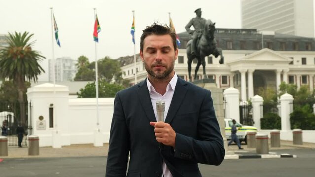 A journalist in a business suit gives an interview in front of the South African flag in South Africa. professional male reporter at work. man standing on the street with a microphone