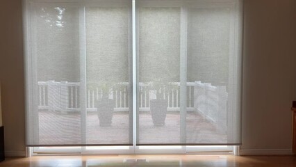 4K video of motorized roller shades in home living room interior being raised. Automatic beige color roller shades are battery powered via remote or smartphone control