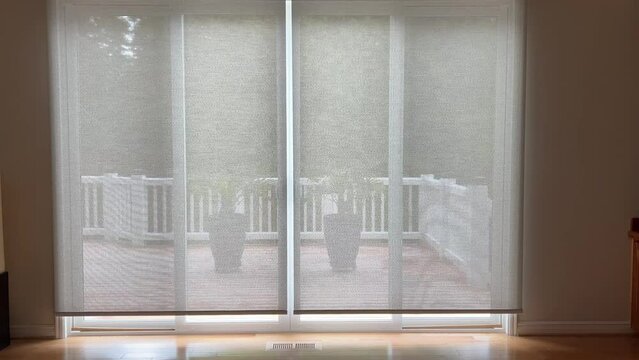 4K video of motorized roller shades in home living room interior being raised. Automatic beige color roller shades are battery powered via remote or smartphone control