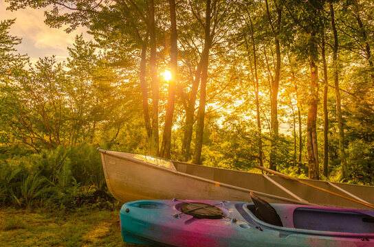 A kayak and canoe in front of trees with sunset