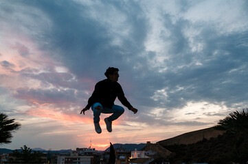 Silhouette of a person jumping outdoors with the sunset sky on background.