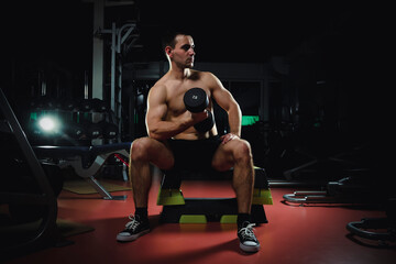Fototapeta na wymiar handsome muscular sportsman lifting dumbbell while sitting in gym