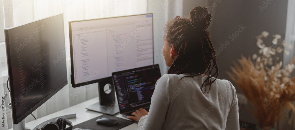 Wall mural rear of young woman looking at computer screen while working programming on laptop