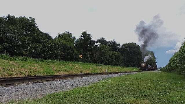 A Low Angle of a Steam Passenger Train Starting Up With Puffs of Smoke and Steam on a Sunny Day