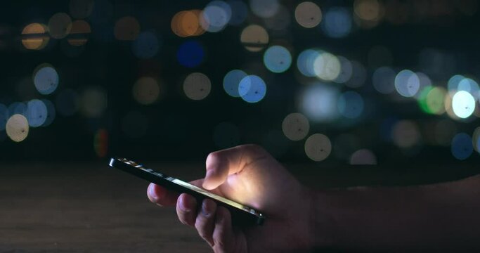 Male hand scrolling browsing on a smartphone at night time. Close-up of person using smartphone, browsing social network. Cinematic shot of male hand scroll through news feed on app on his smartphone.