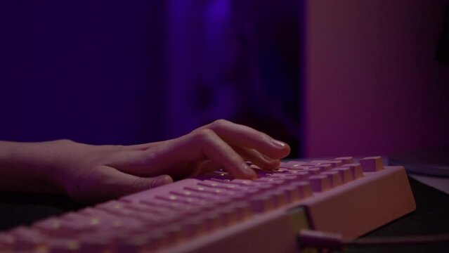 Close-up of fingers pressing on keyboard during game. Stock footage. Pink glowing keyboard for computer games. Fingers press game keys of computer keyboard
