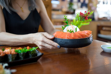 Woman holding salmon sashimi in black bowl on wood table background, Japanese style - obrazy, fototapety, plakaty