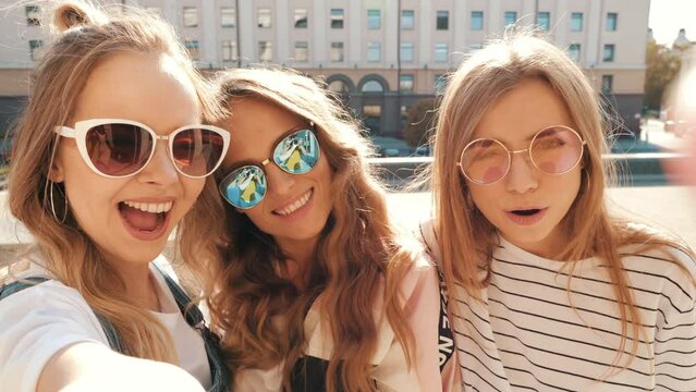 Three young smiling hipster women in summer clothes. Girls taking selfie self portrait photos on smartphone. Models posing in the street. Female showing positive face emotions