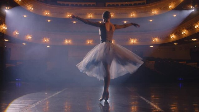 Ballet female dancer in white tutu dress practices choreography moves on stage and prepares to start a show. Ballerina on rehearsal of performance. Illuminated theatrical hall. Classical ballet art.