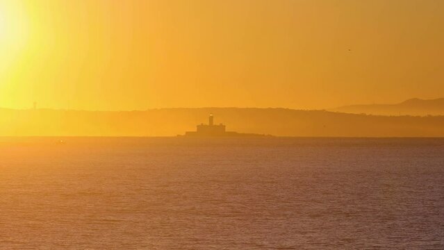 high-quality footage shows the picturesque Lisbon coast under a sunrise sky, featuring the prominent Forte do Bugio lighthouse set offshore