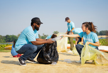 A diverse group of volunteers join together to cleanup the sand beach,collect garbage,separate...