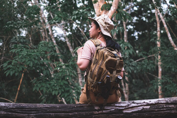 Back view of woman with backpack hiking sitting on a tree trunk in deep forest