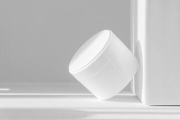 Mockup of white jar for packaging cosmetics on isolated background. Container with moisturizer without marking close-up against white wall, in rays of sunlight. Concept of skin care, rejuvenation