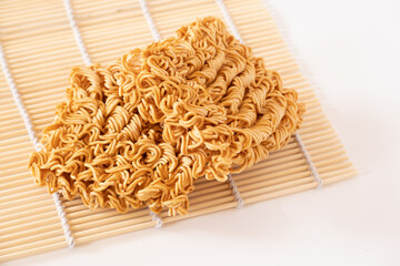 Instant noodles, a dried and precooked noodle block on bamboo mat isolated on white background.