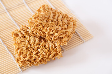 Instant noodles, a dried and precooked noodle block on bamboo mat isolated on white background.