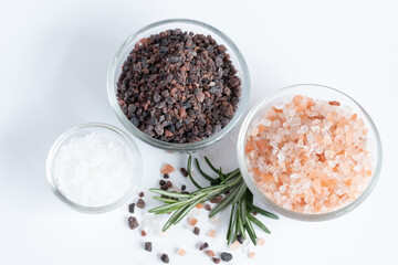Top view of variety of different flake flower sea salt, Himalayan black salt and pink Himalayan with rosemary for cooking or spa on white background.