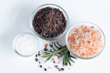 Top view of variety of different flake flower sea salt, Himalayan black salt and pink Himalayan with rosemary for cooking or spa on white background.