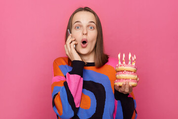 Amazed news on birthday. Shocked astonished female in colorful sweater holding delicious sweets...