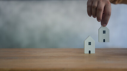 Hand man choosing one mini wood house model from two model on wood table, planning to buy property....