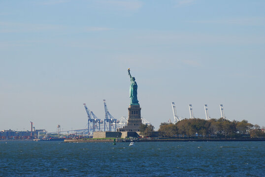 Statue of Liberty and Liberty Island with cranes in background in New York, USA