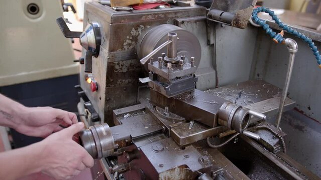An engineer turns a handle as he shaves metal from a larger metal bar on a metal turning lathe. The metal in question is a steel and aluminium alloy. Shot in Stornoway on the Outer Hebrides, Scotland.