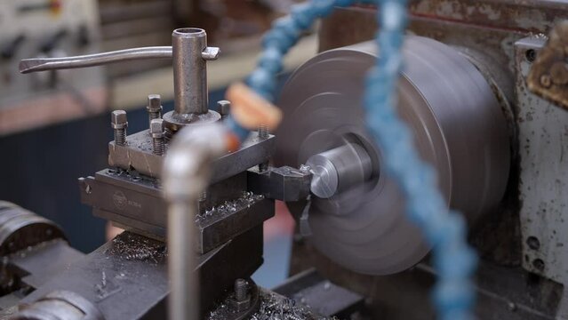 Shot of metal shavings being gradually removed from an iron bar on a metal turning lathe. An engineer is turning the handle. The spindle, chuck, tool post and stock are visible. Shot in Stornoway.