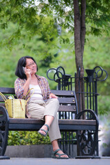 Asian woman sitting on park bench on the roadside of Malioboro street, making a phone call