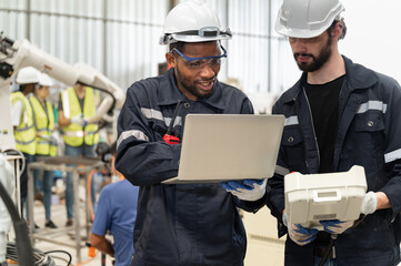 Caucasian and African American technician engineer man use remote control and computer notebook with checking machine arm robot at factory	