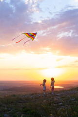 two happy little kids boys having fun with kite in nature at sunset