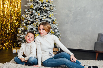 Obraz premium holiday mother and son sit by the tree new year christmas