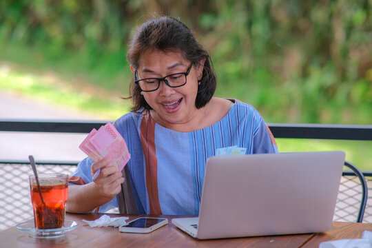 Asian female entrepreneur sitting at home counting some money in her hands