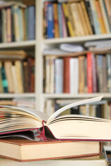 Open book or textbook on a pile of closed books in front of a bookcase in a library. Education learning concept. Image with selective focus.	