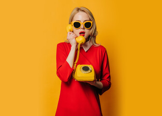 Stylish surprised woman in red dress with dial phone on yellow background
