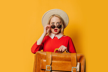 Surprised blonde hair woman in red dress with suitcase on yellow background