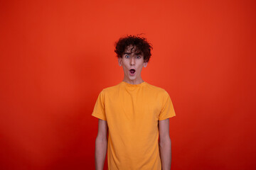 Young attractive guy posing in the studio. Emotional man. Orange background.