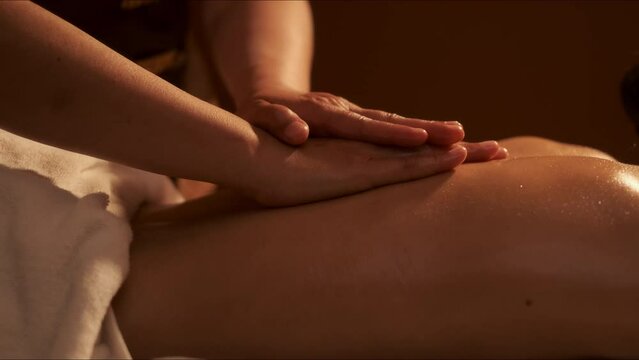 Hand of masseuse doing massage back with aromatherapy oil on back of a woman customer in spa salon.