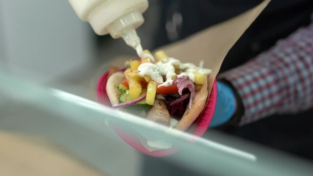 Cook pouring white tzatziki sauce on a gyros sandwich in a Greek restaurant kitchen