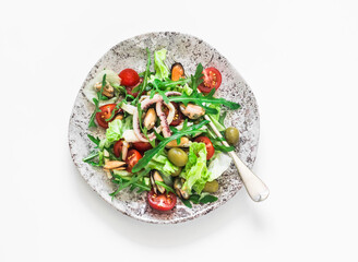 Salad with arugula, cherry tomatoes and seafood on a light background, top view