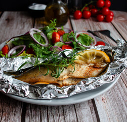 Mackerel baked in foil with vegetables on a plate. on a wooden background